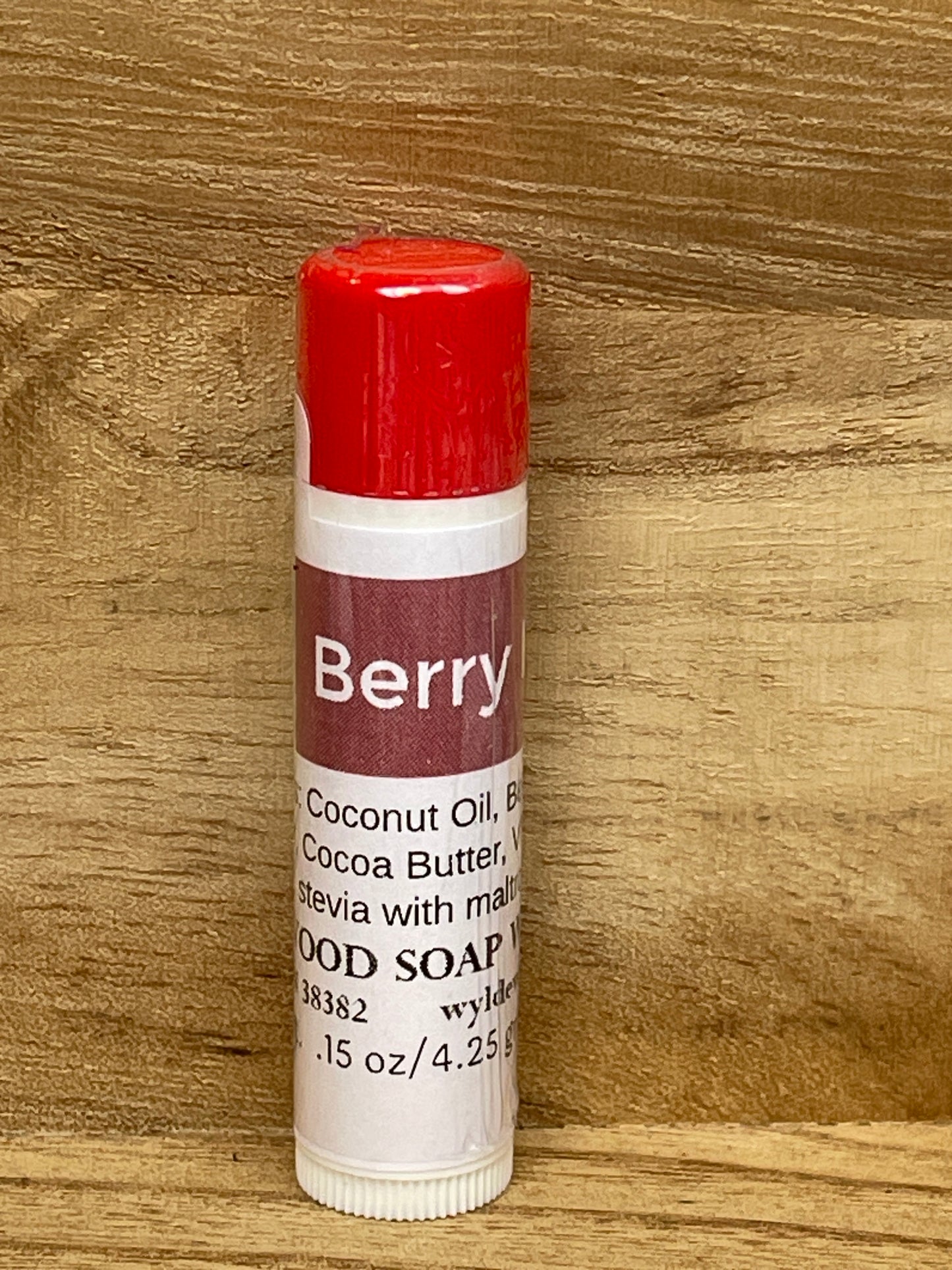 Three tubes of Berry Mint flavor lip balms made by Wyldewood soap works standing on a wood background.