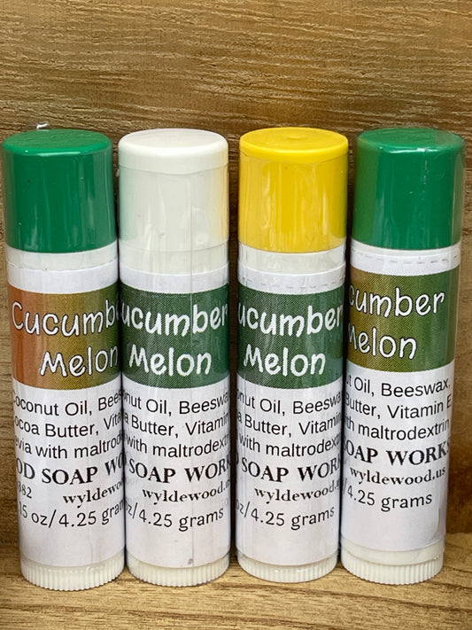 Three tubes of Cucumber Melon flavor lip balms made by Wyldewood soap works standing on a wood background.