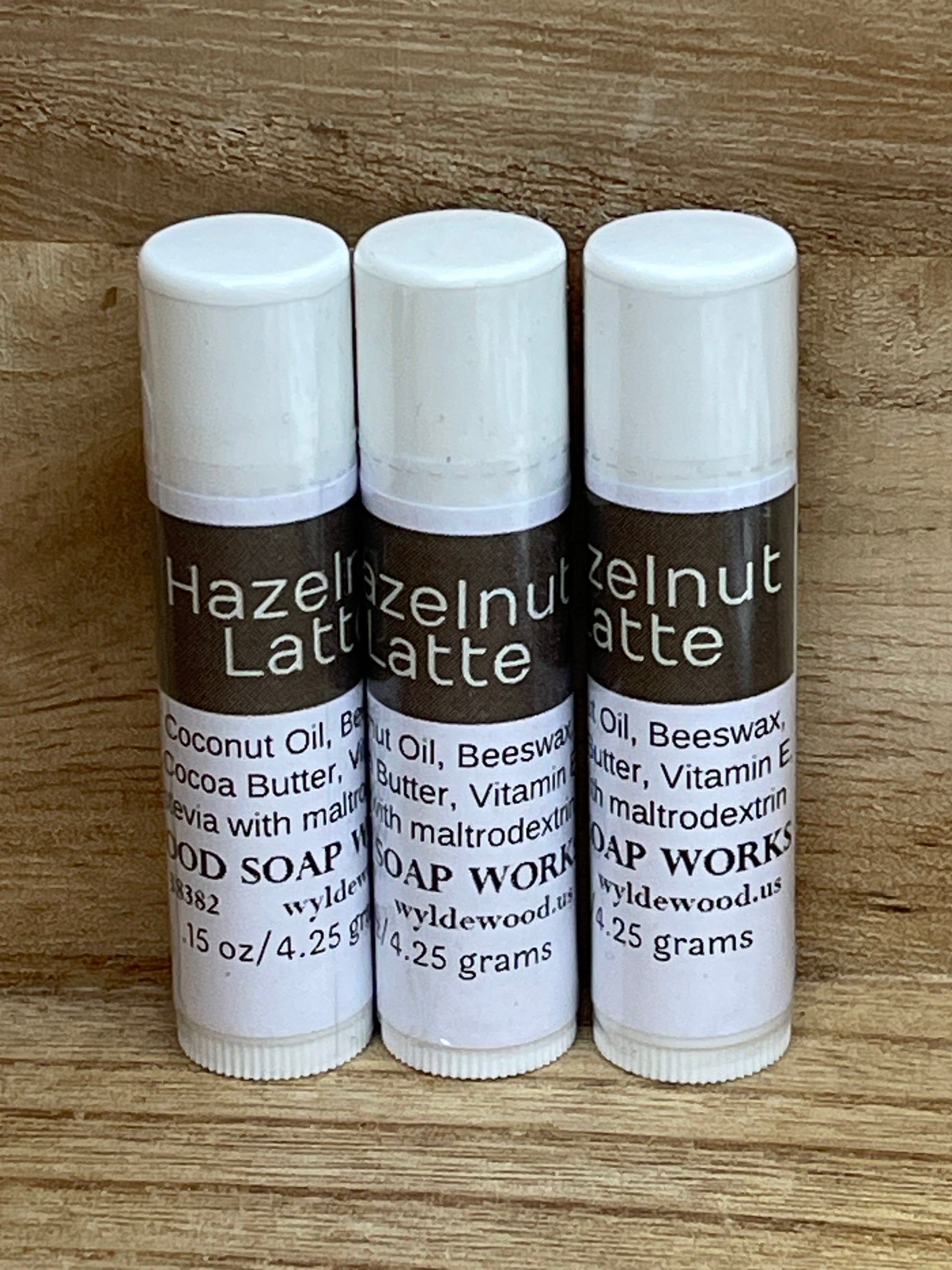 Three tubes of Wyldewood Soap Works lip balm standing up on a wood grain background.