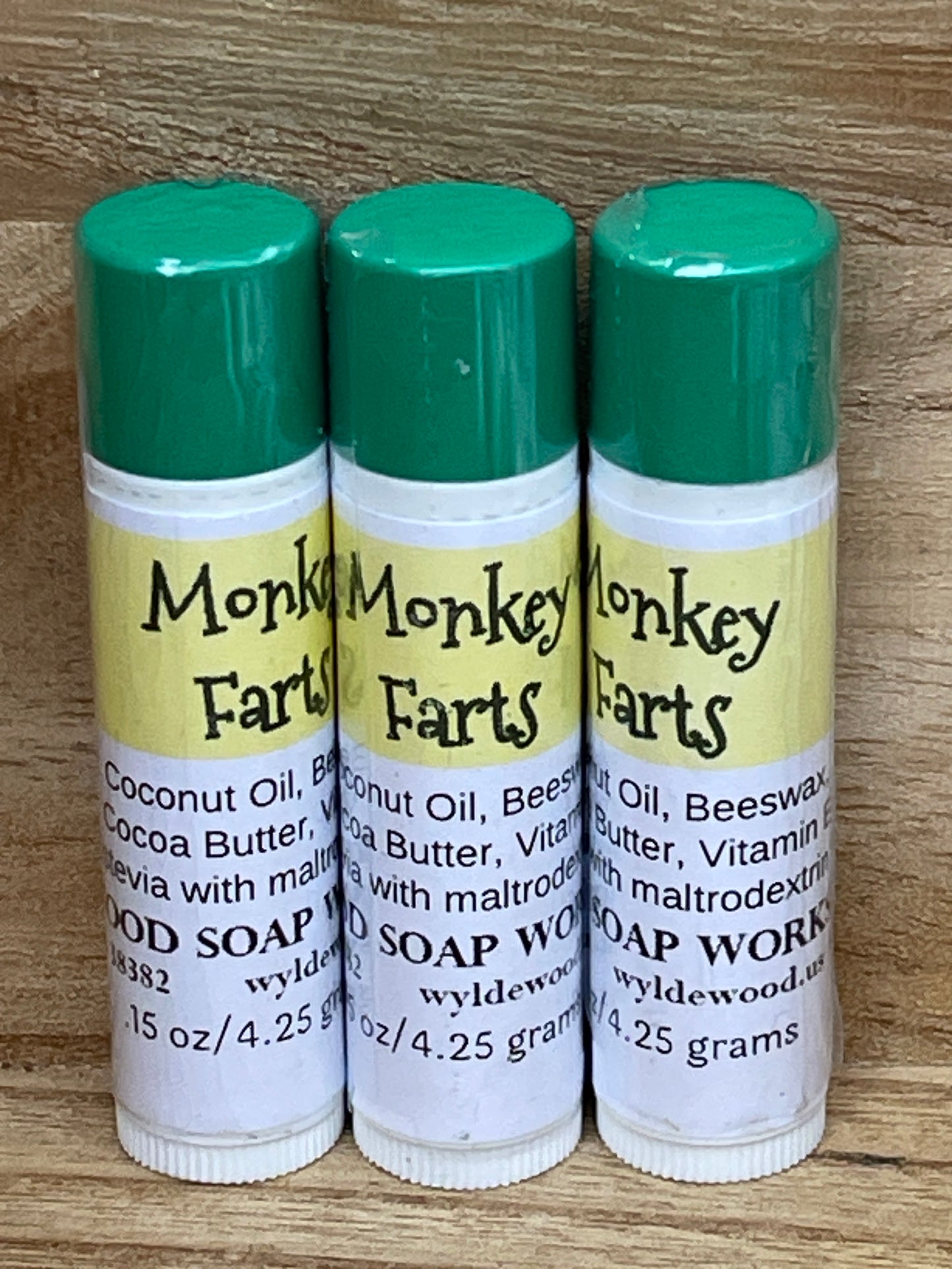 Three tubes of Monkey Farts flavor lip balms made by Wyldewood soap works standing on a wood background.