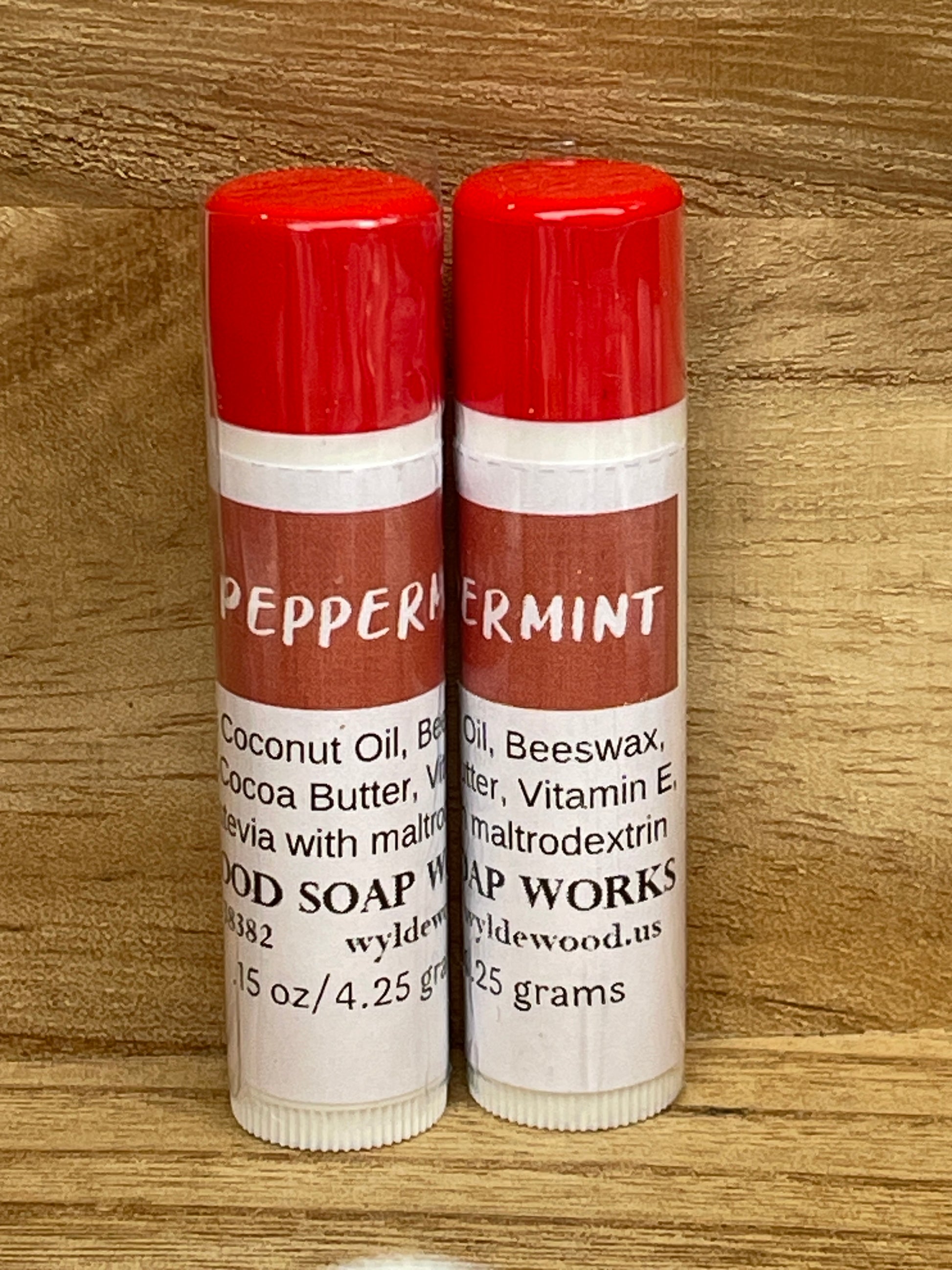 Three tubes of Peppermint flavor lip balms made by Wyldewood soap works standing on a wood background.