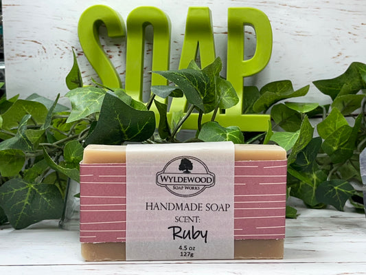 A bar of handmade soap with packaging that has 'WYLDEWOOD HANDMADE SOAP' and the scent listed as 'Ruby'. The bar is placed on a white surface with leaves in the background.