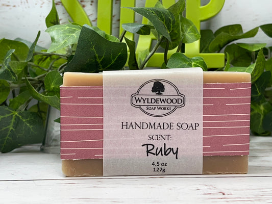 A bar of handmade goat milk soap with 'Ruby' scent, packaged in a pink and white striped wrapper with a label that includes the brand name 'Wyldewood', the product name 'Ruby Scented Soap', and the weight '4.5 oz / 130 g'.