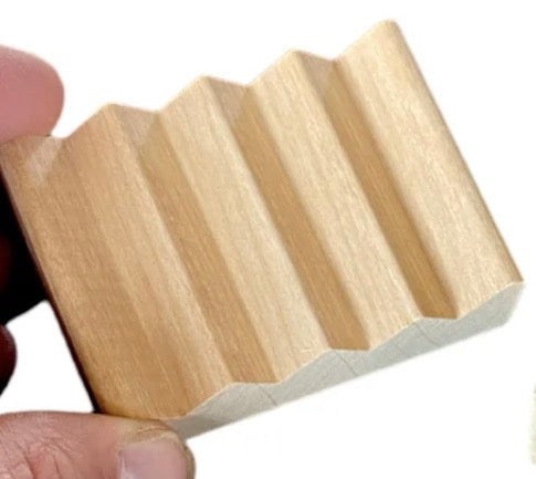 Fingers holding a wooden soap dish that has large ridges to allow water to drain away from the soap.